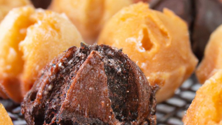 Imagem de um petit gateau de chocolate feito na Airfryer. O bolo é pequeno e redondo, com uma cobertura de chocolate derretido. O interior do bolo é úmido e cremoso, com um centro derretido. O bolo é servido em um prato branco com uma colher ao lado.