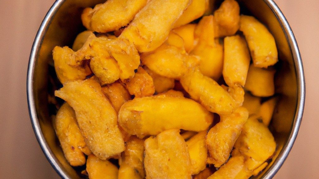 Foto de uma tigela de macaxeira frita, servida com molho à parte. A macaxeira é cortada em pedaços pequenos e frita até dourar. O molho é feito com tomate, cebola e pimentão.