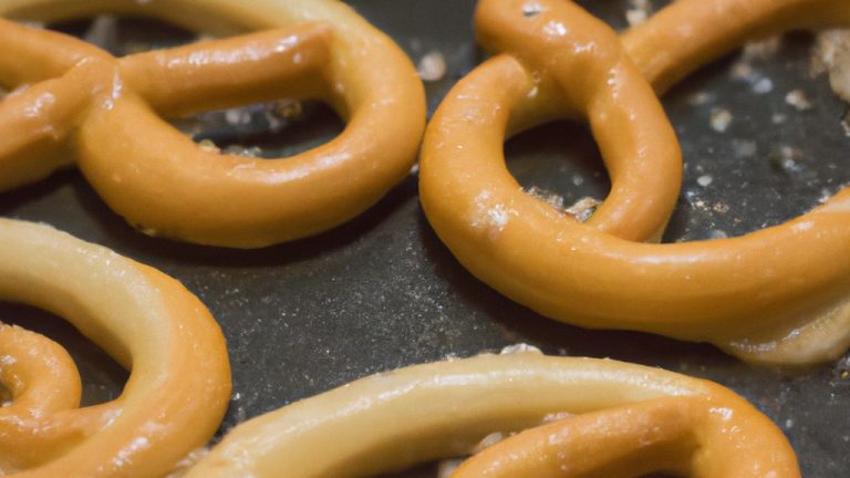 Imagem de pretzels crocantes e dourados feitos na fritadeira sem óleo. Os pretzels são dispostos em uma tigela de cerâmica branca, com sal grosso polvilhado por cima. O fundo da imagem é uma superfície texturizada de madeira escura, criando um contraste visual.